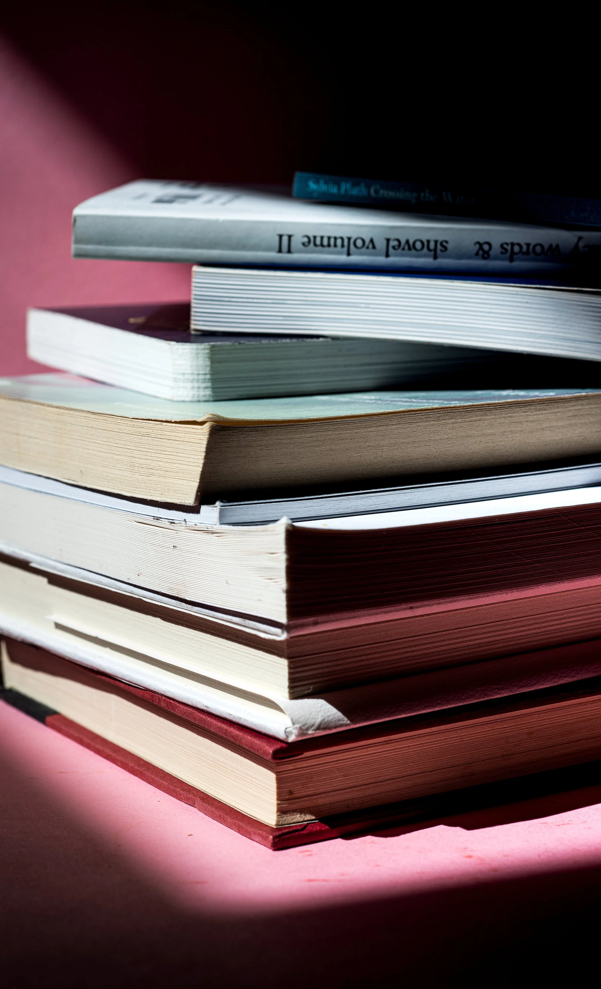 Stack of books on a pink surface with shadows and a pink background.