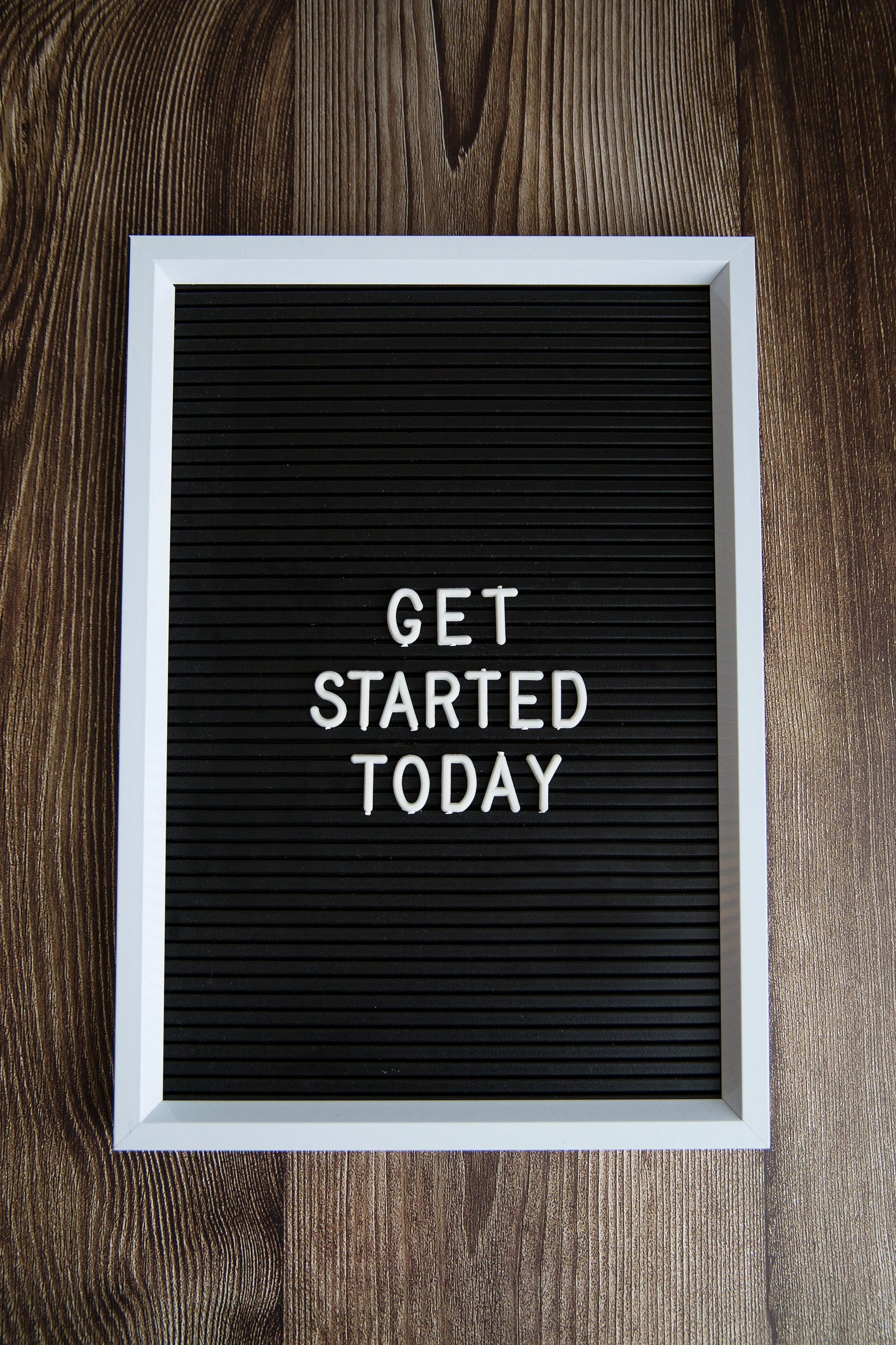 Black felt letter board with white frame displaying the message "GET STARTED TODAY" on a wooden surface.