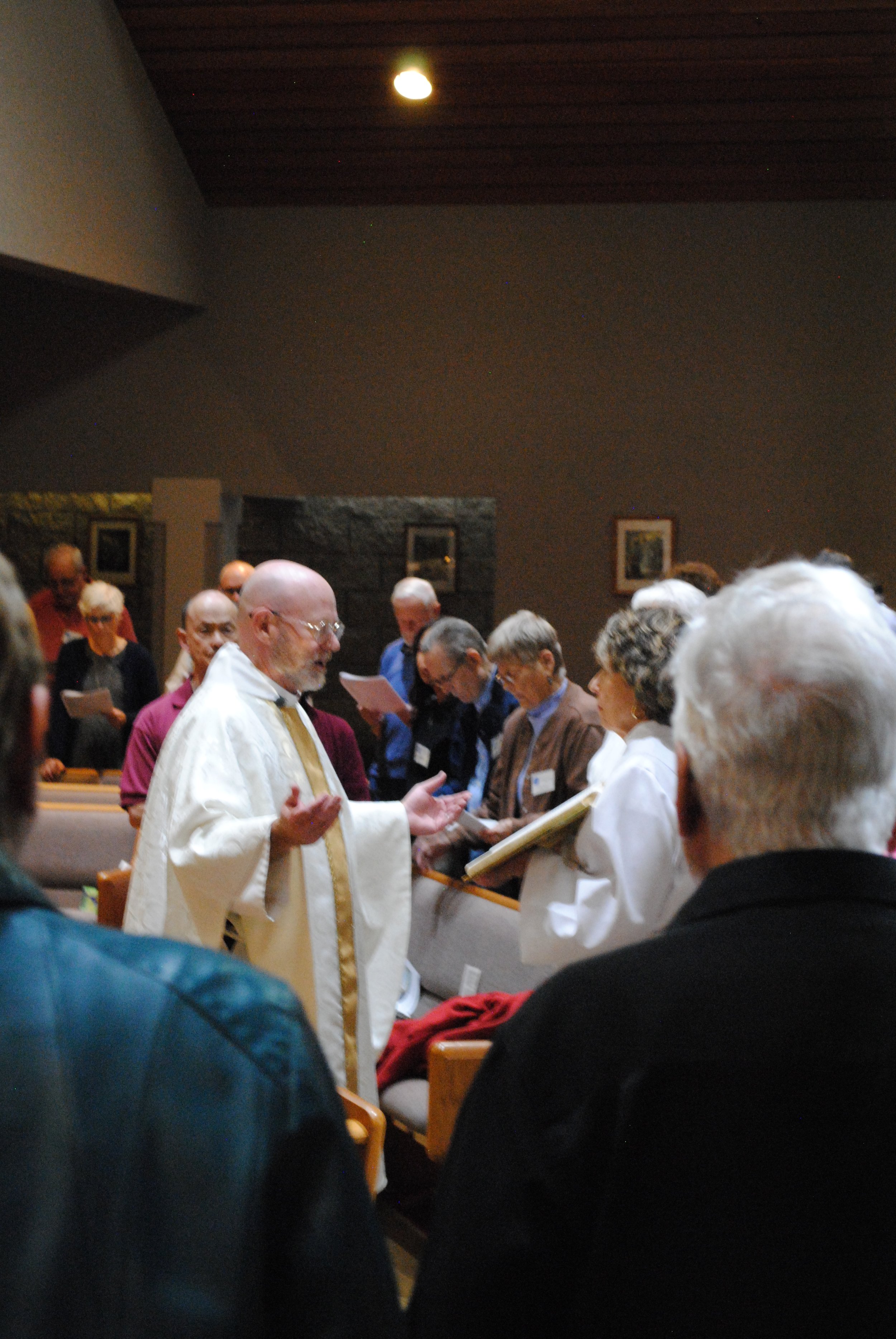 A group of people gathered in a church, participating in a religious ceremony, with a priest in white robes leading the service.
