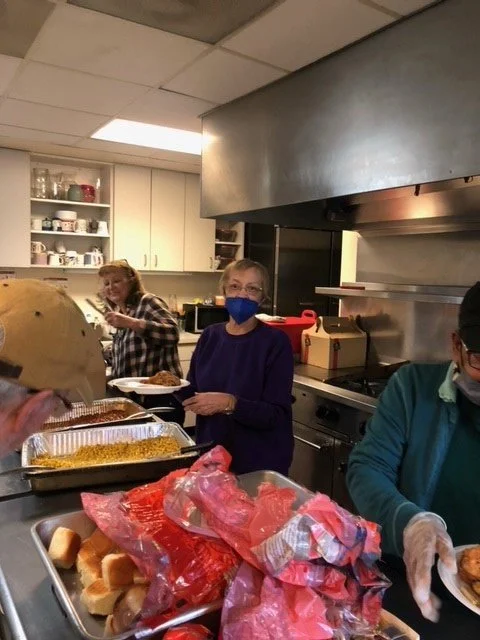 Group of people serving food in a kitchen with baked goods and baked items on the counter.