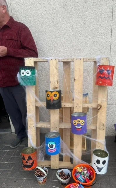 Decorative Halloween-themed craft display with painted tin cans resembling monsters and pumpkins, decorated with yarn, cotton balls, and plastic spider web accents.