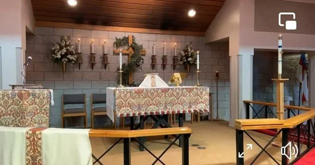 Church altar decorated with candles, flowers, and a cross, set for a religious service.