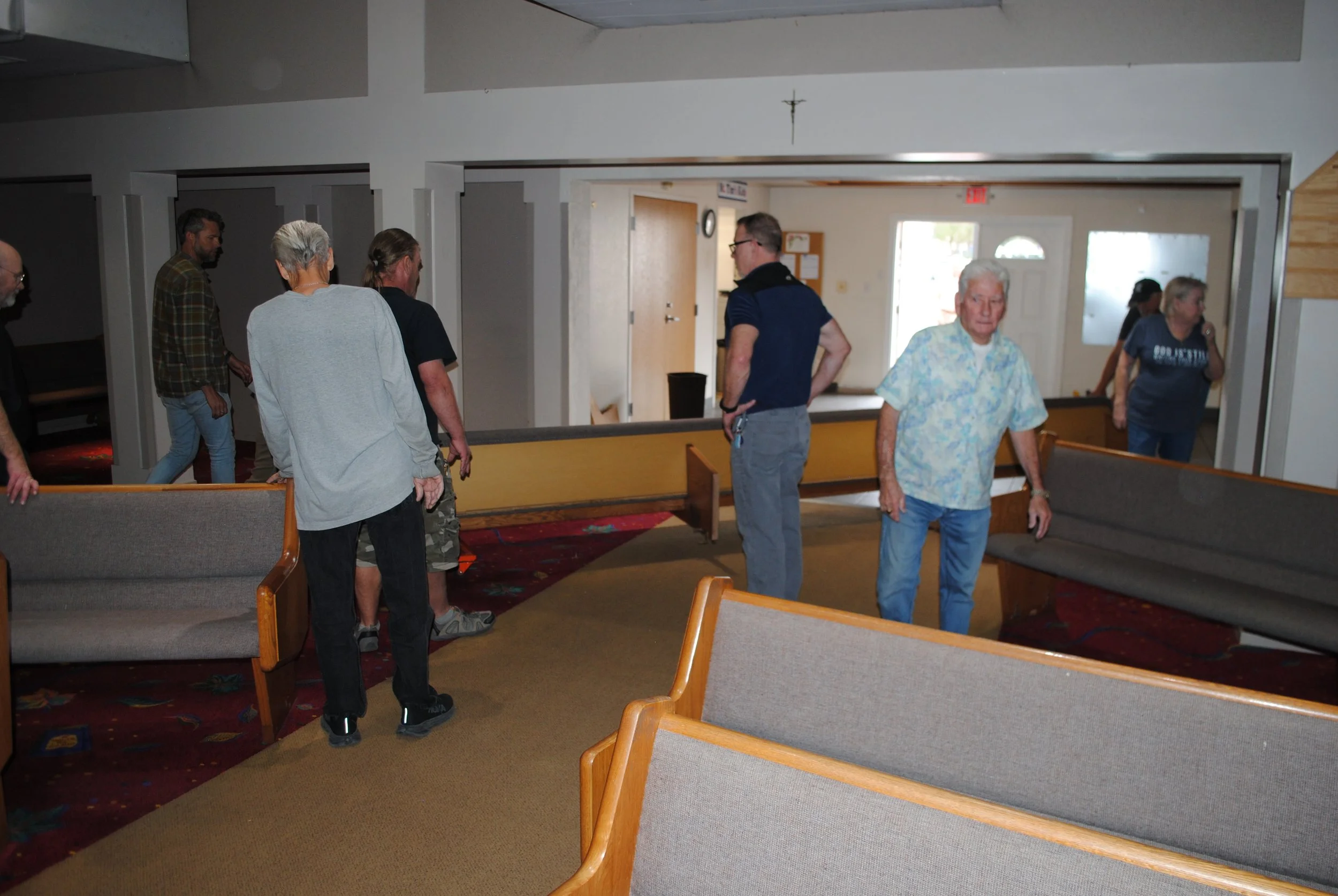 A group of people standing and walking inside a church with wooden pews and carpeted floors.