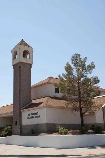 A church building with a tall bell tower, labeled 'St. Timothy's Episcopal Church,' with a tree and a clear blue sky in the background.