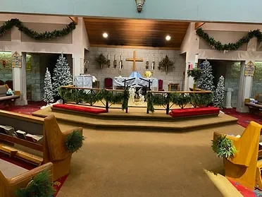 Interior of a church decorated for Christmas with garlands, Christmas trees, and pews decorated with greenery.