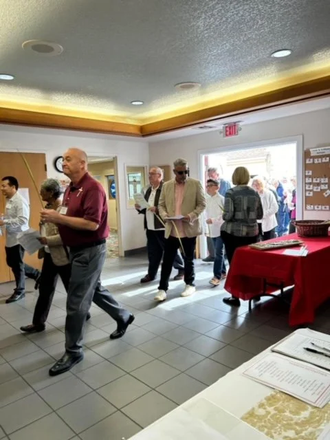 People entering or waiting in line at a social or networking event in a room with a red tablecloth and informational displays.