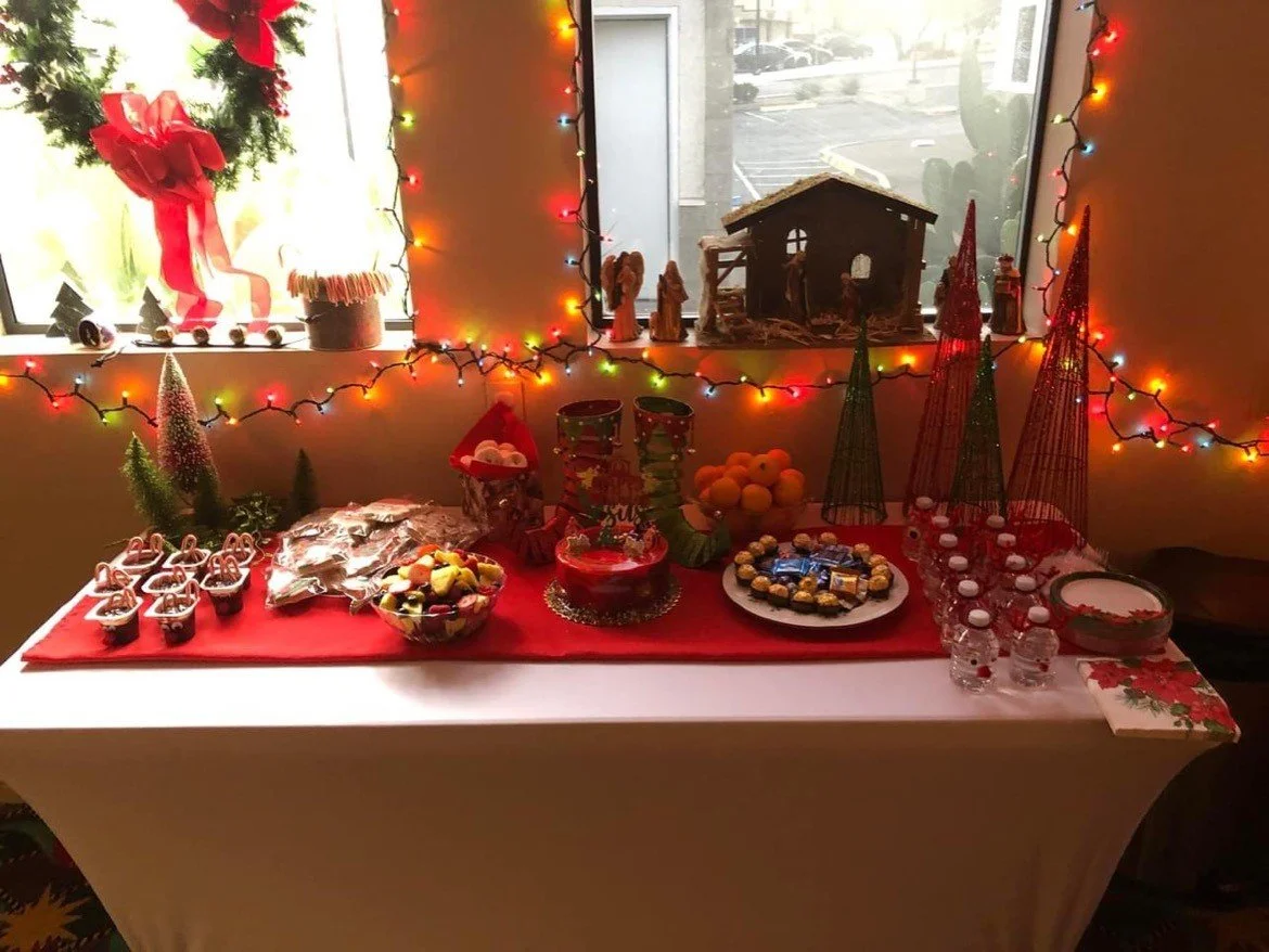 Christmas-themed dessert table with candy, cookies, and Christmas decorations, illuminated by colorful string lights.