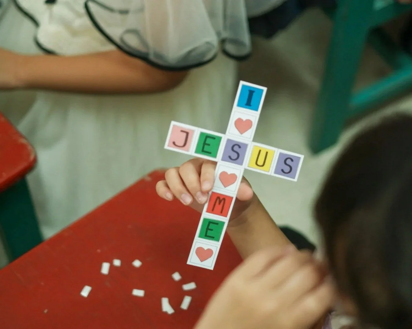 Child holding a colorful cross-shaped paper craft with the words 'I love Jesus.'