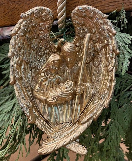 Decorative ornament of a nativity scene with angels, set among Christmas greenery.