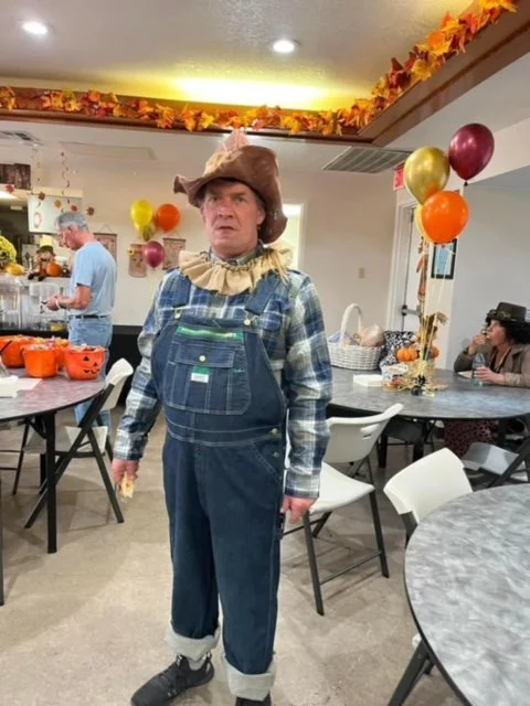 Person dressed as a scarecrow in a decorated room with balloons and autumn-themed decorations.