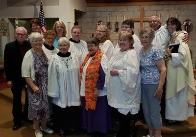 Group of people, mostly women, gathered indoors with an American flag in the background, dressed in church or community attire, smiling for the photo.