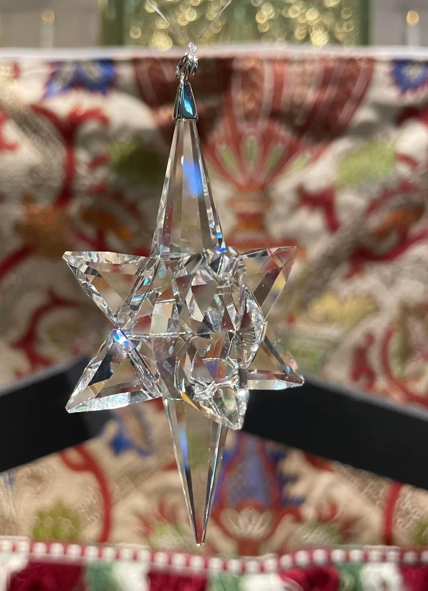 Close-up of a crystal star-shaped ornament in front of a Christmas-themed background with wrapped presents.
