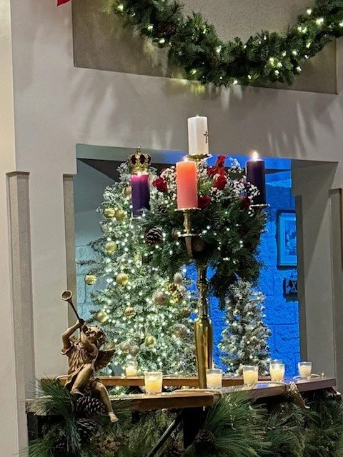 Christmas decorations featuring a lit Christmas tree, candles, and a wreath reflected in a mirror.