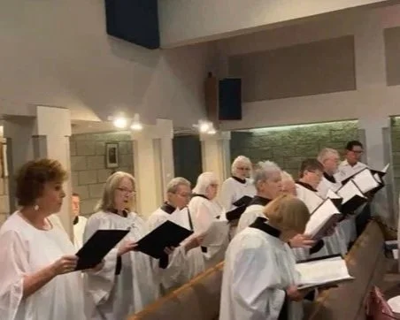A choir of elderly people singing from sheet music in a church.