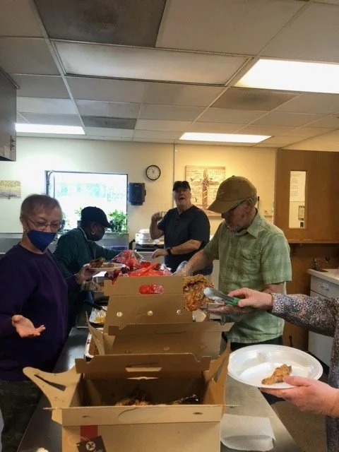 People serving and receiving food in a community kitchen or food pantry.