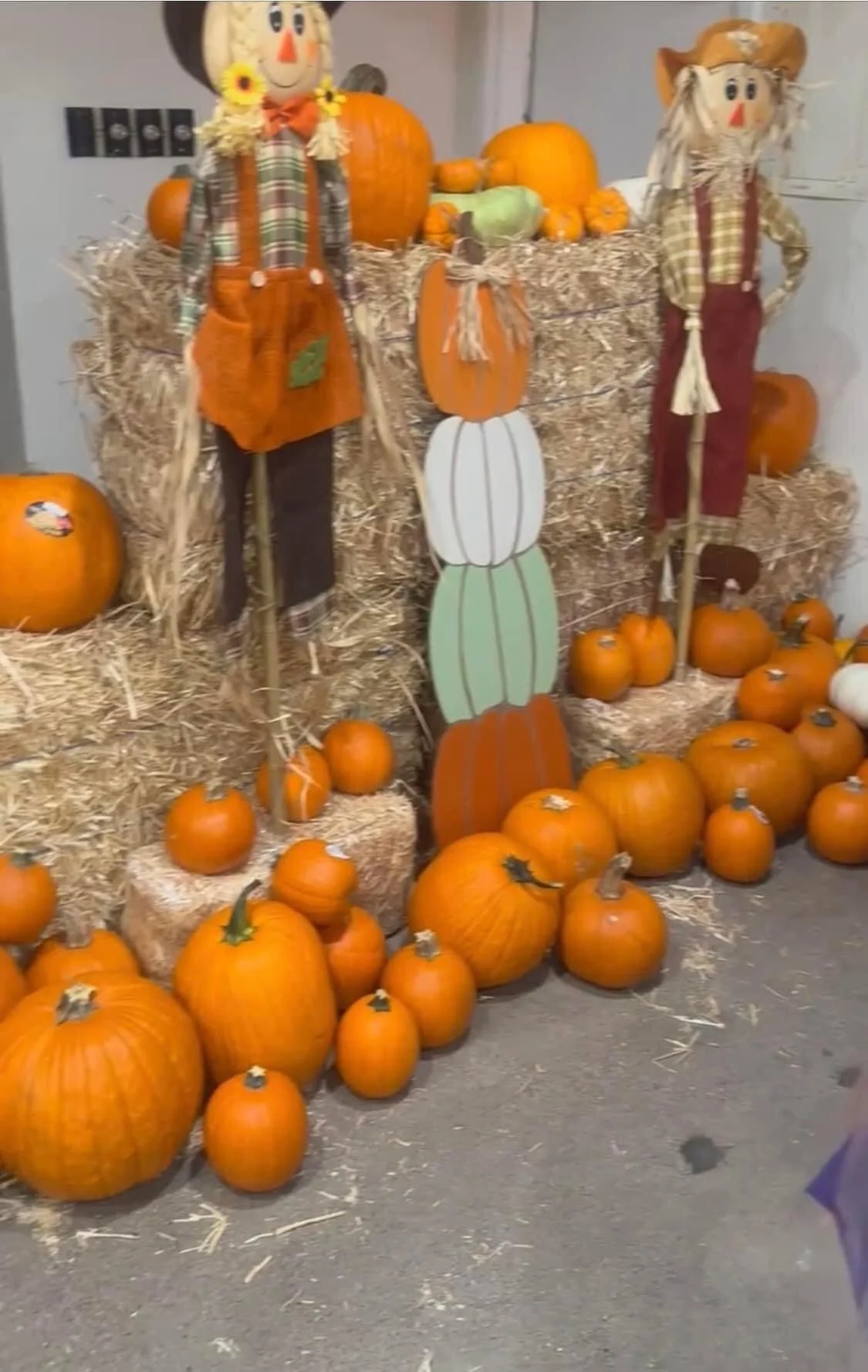 Fall harvest display with pumpkins, straw bales, and scarecrow figures.