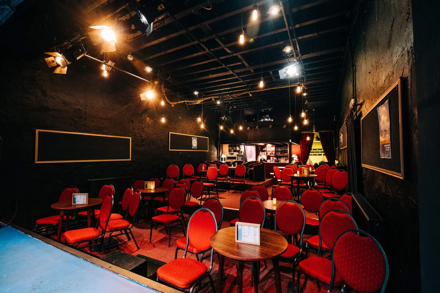 Een donker coffeehouse met rode stoelen en tafels, zachte verlichting en een bar op de achtergrond.