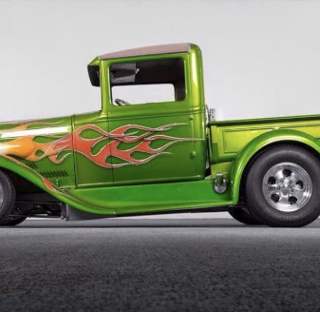 A bright green vintage pickup truck with orange and yellow flame decals on the side, parked indoors.