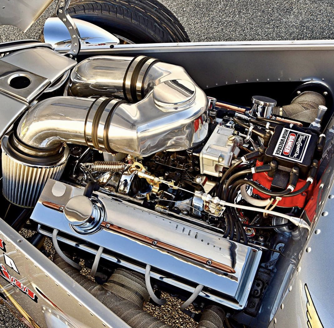 Close-up view of a high-performance race car engine with polished metal components, a large air intake, and a red valve cover.