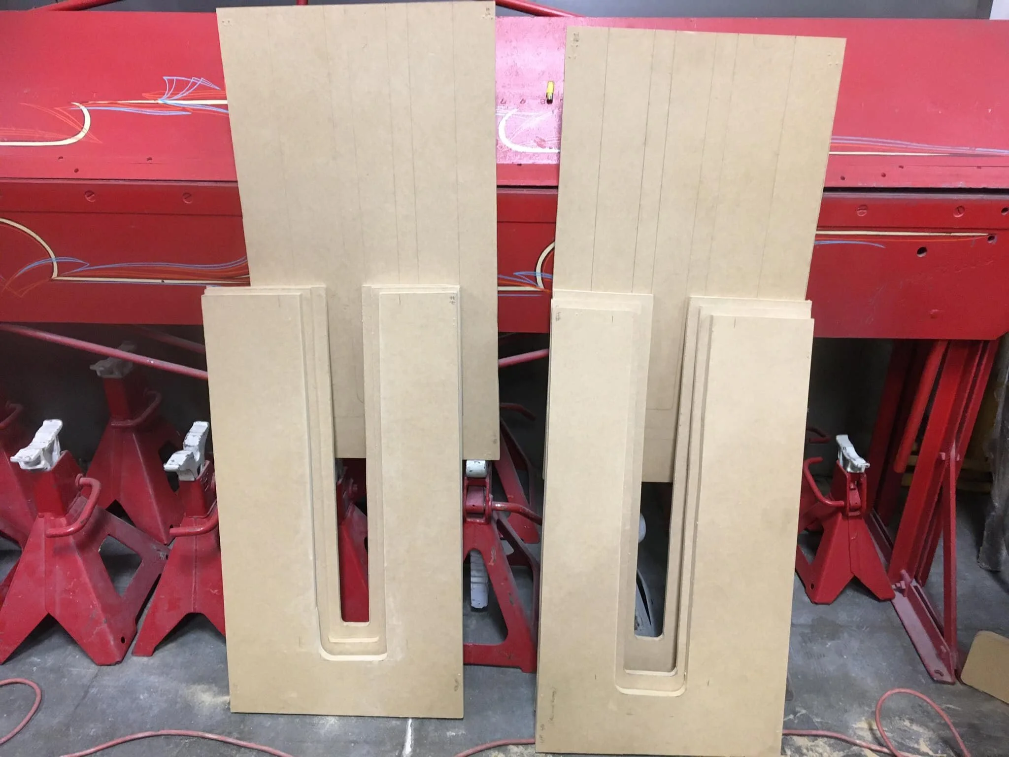 Two large beige wooden panels with rectangular cutouts, standing upright in front of red workbenches and scaffolding in a workshop