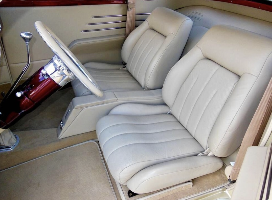 The interior of a vintage car showing beige leather seats, a steering wheel, and a gear shift.