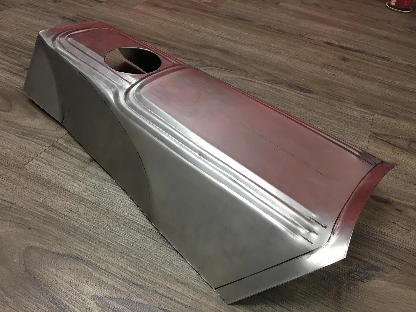 Metal car hood with a circular hole, placed on a wooden floor.