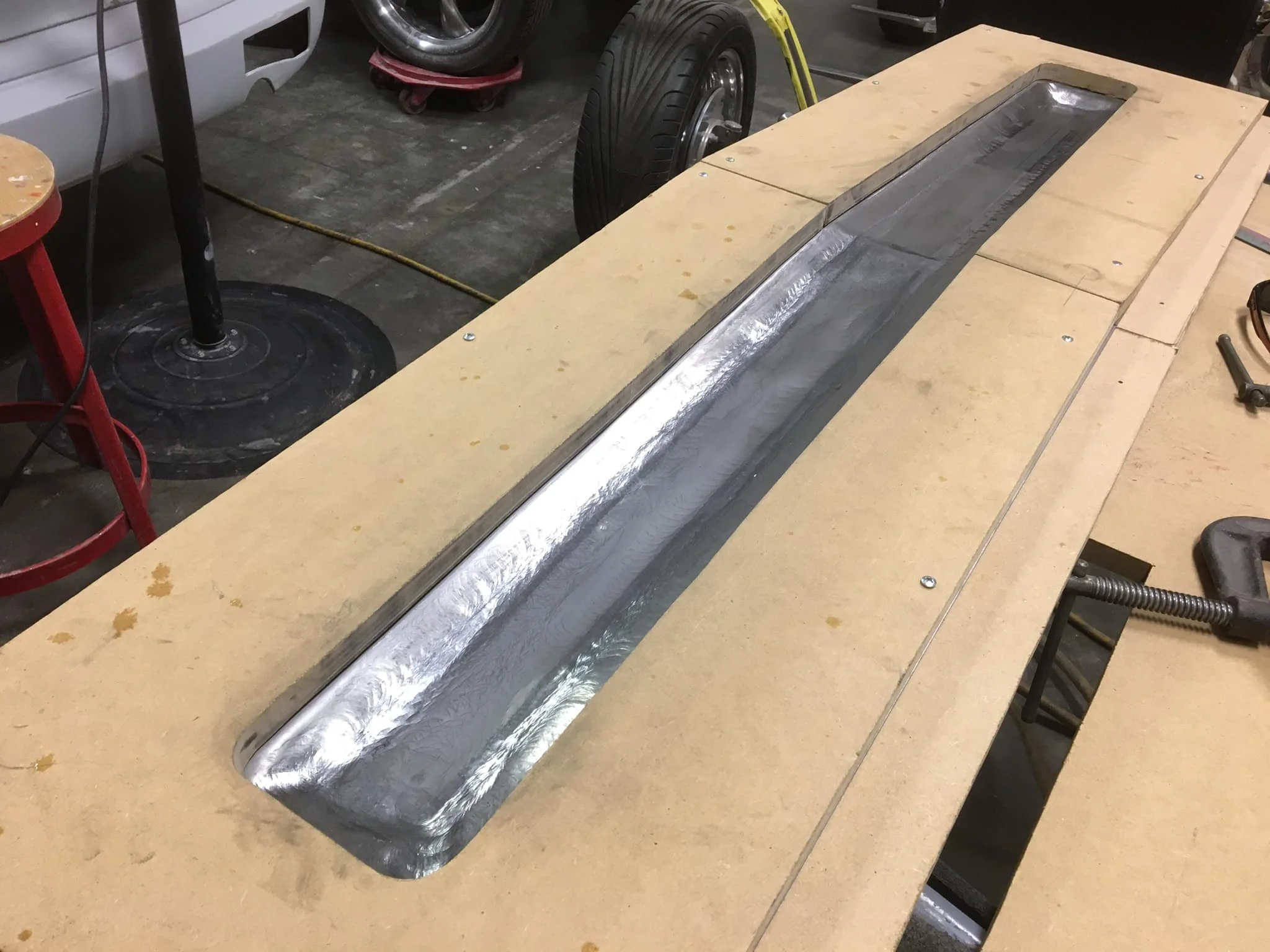 Metallica channel with a long, rectangular, slightly curved metal trough placed on a wooden workbench in a workshop.