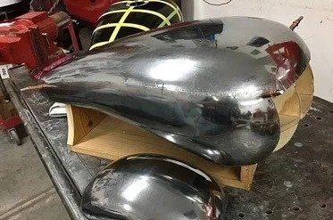 A shiny, metallic teardrop-shaped object on a wooden stand, next to a similar smaller metallic piece.