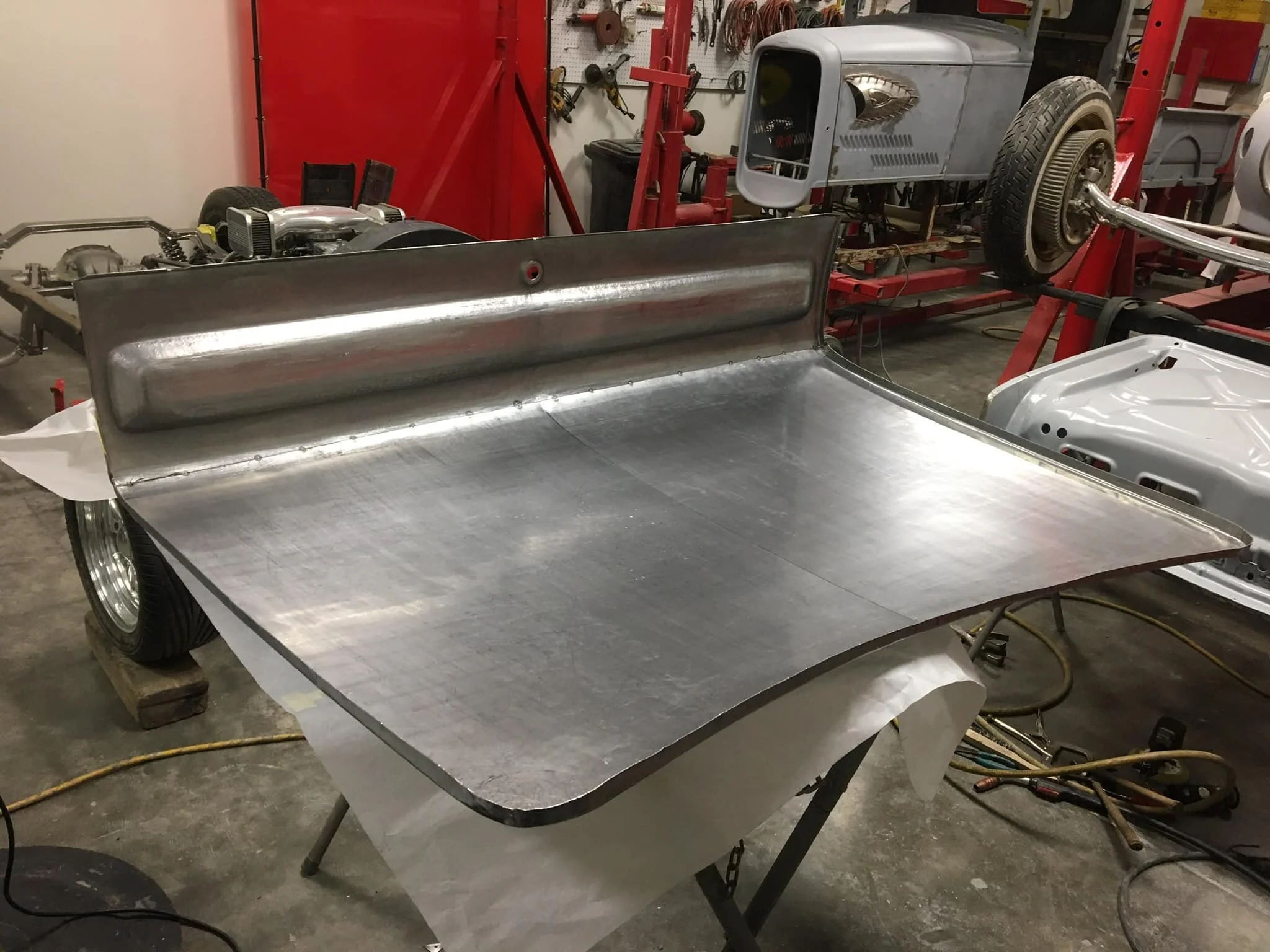 A metal car dashboard being fabricated in a workshop, surrounded by various car parts and tools.