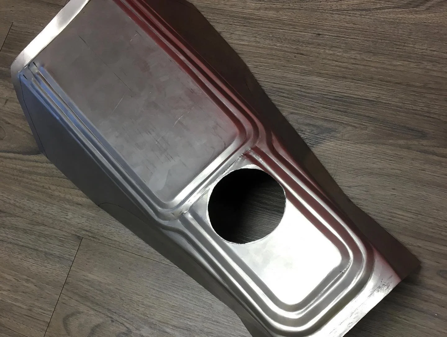 Stainless steel trash bin with an open cylindrical hole on the top, placed on a wooden floor.