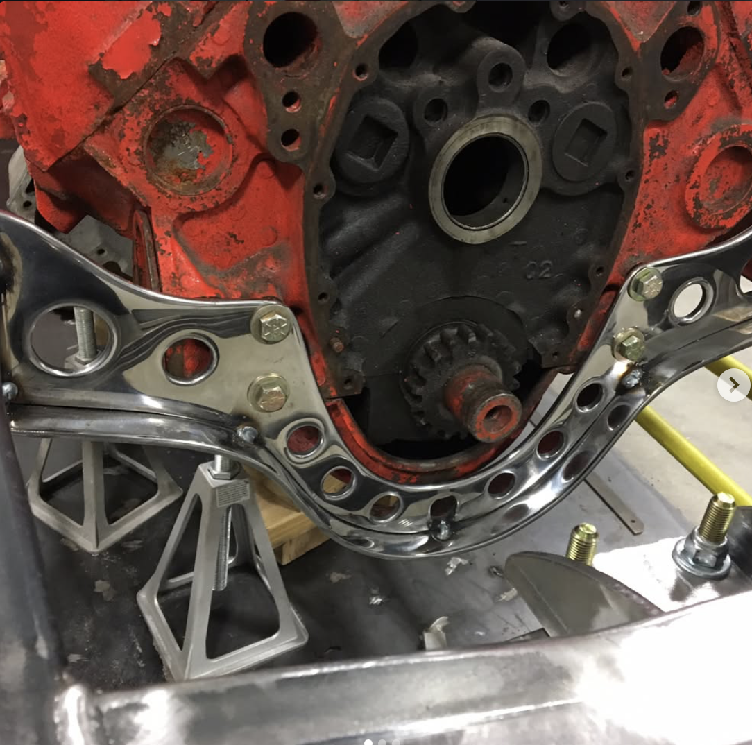 Close-up of a red engine block with mounting brackets and a timing gear, partially disassembled with support stands underneath.