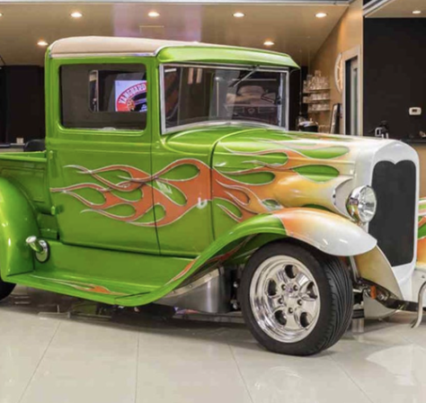 A vintage green truck with orange and yellow flame decals on its sides, parked indoors.