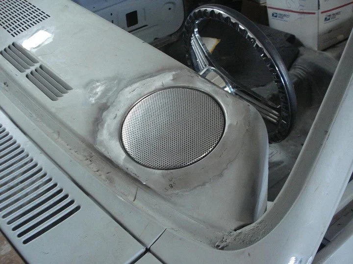 Close-up of a vintage record player with a damaged white surface, a speaker grille, and a chrome turntable in the background.