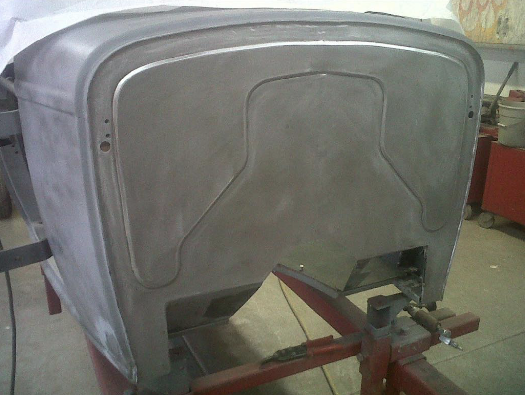 A large, rectangular metal object (possibly a vintage car part or industrial component) is secured on a red work stand in a workshop.