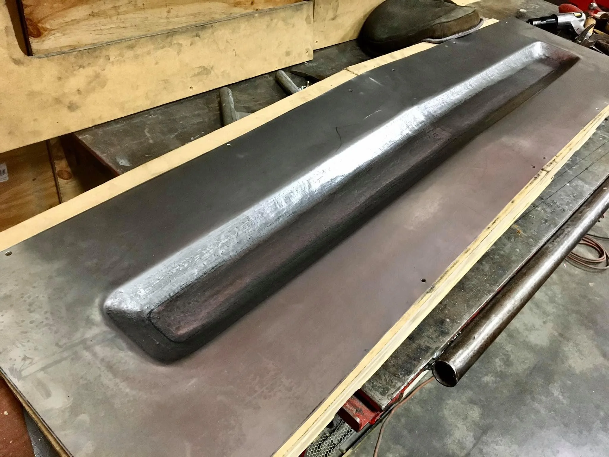 An automotive steel drift or channel, likely part of a custom vehicle or machine, resting on a workbench in a workshop.