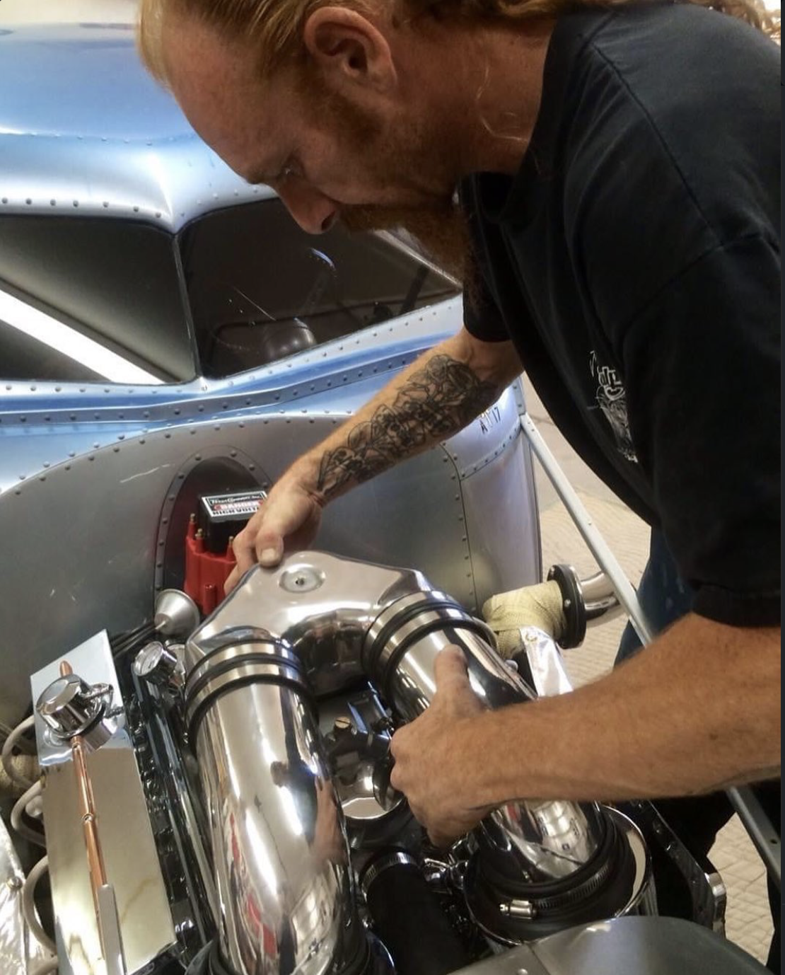 Joe Sulpy working on a vintage race car engine. The car has a metal body and the engine has shiny, chrome components.