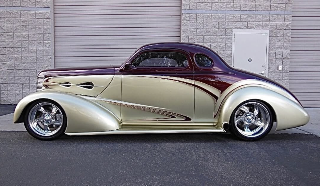 A vintage cream and maroon classic car parked in front of a building with a closed garage door.