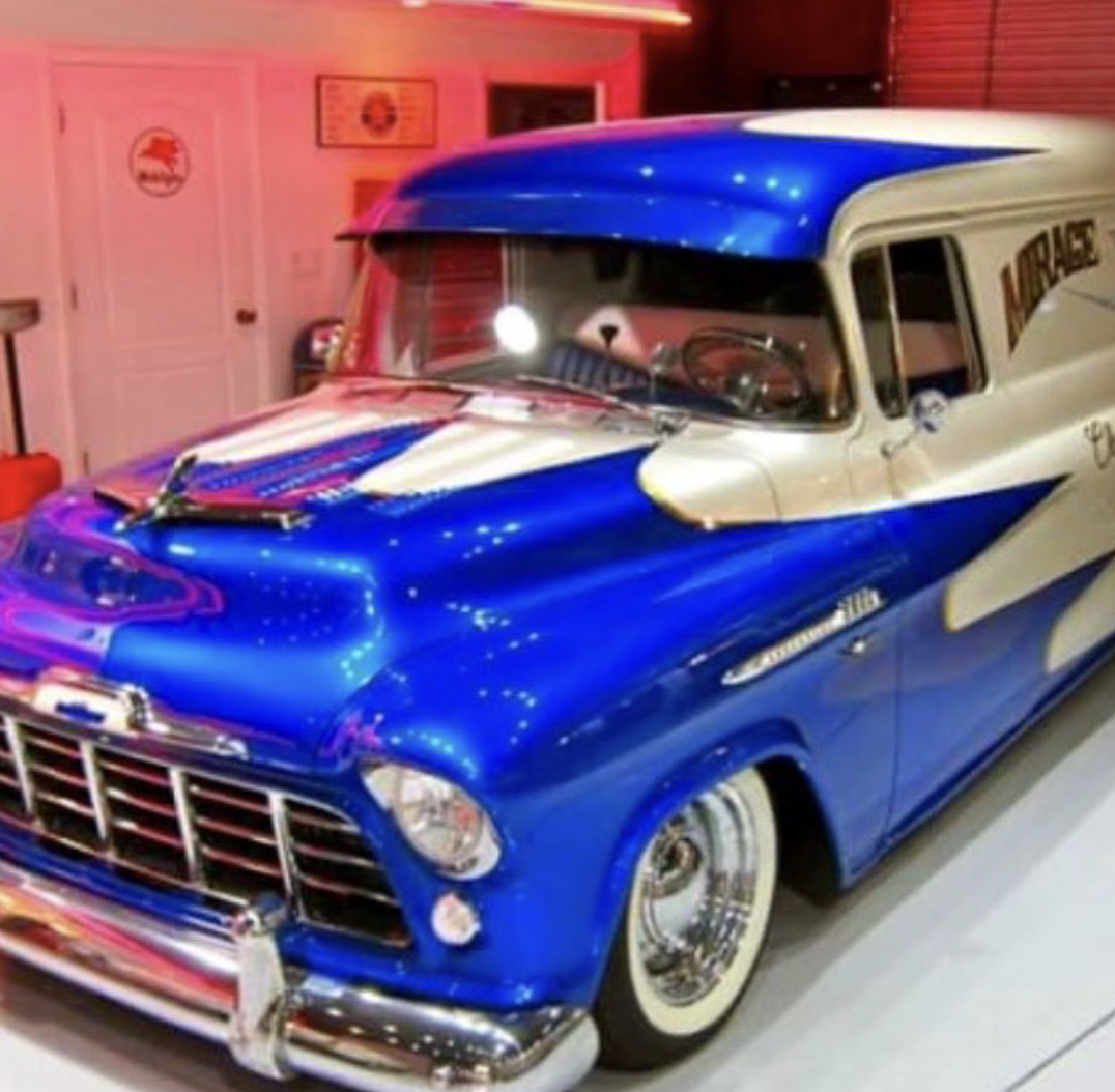 A vintage blue and white car with a classic design, parked inside a room with pink lighting and vintage decor.