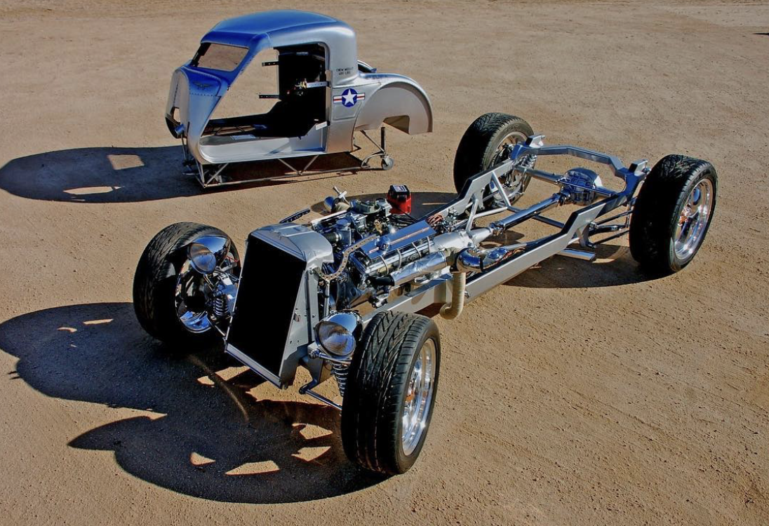 Disassembled vintage car chassis and body with American military star insignia on a sandy surface.