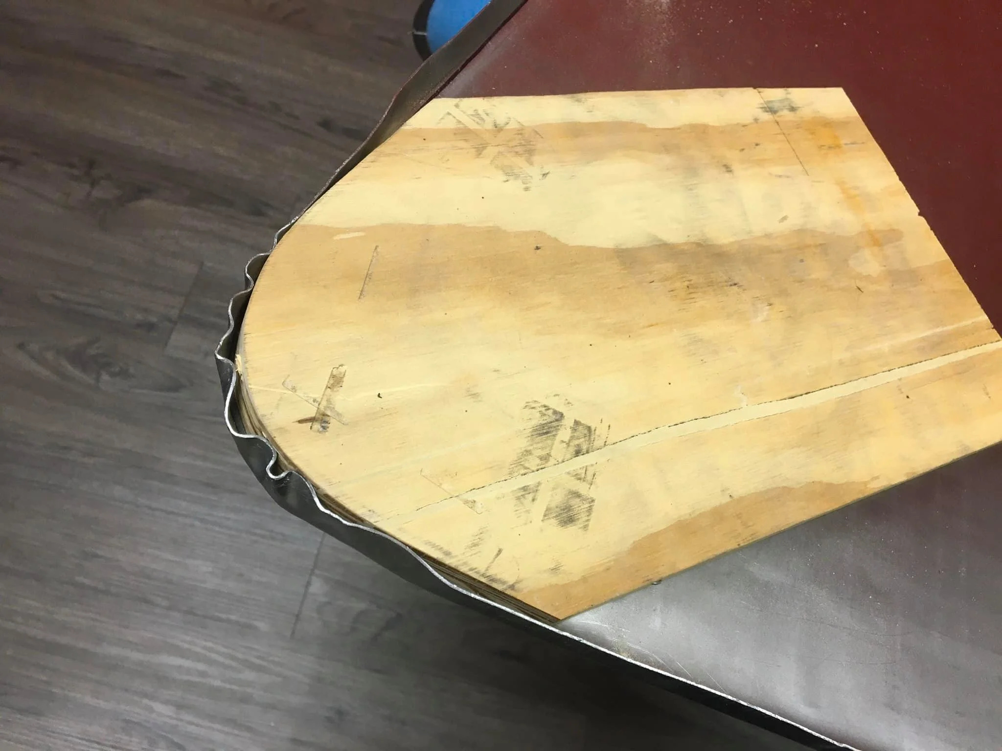 Close-up of a worn, oval wooden cutting board with scratches and stains, placed on a dark surface.