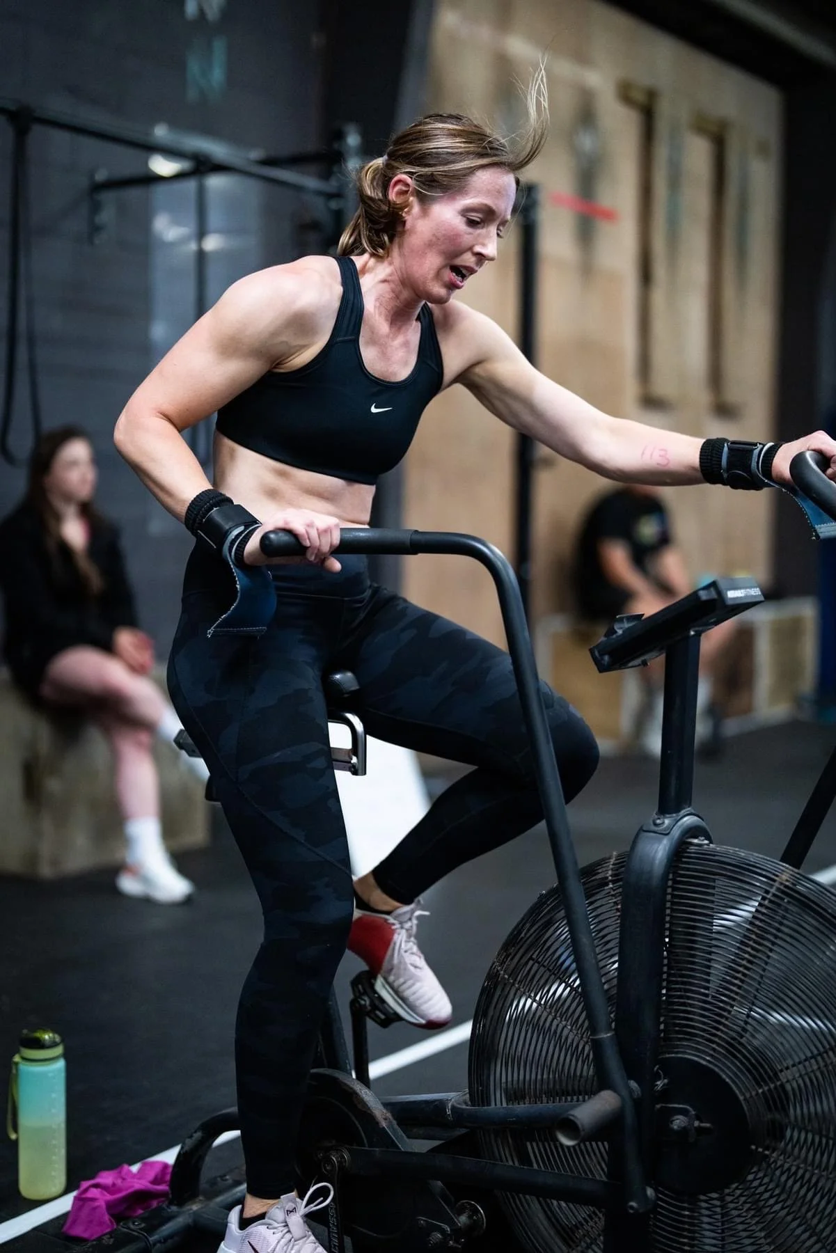 A woman in workout attire is riding a stationary bike in a gym, sweating and focused on her workout.