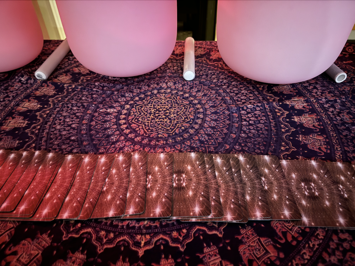 Set of tarot cards with a red and pink starburst pattern, spread out on a dark, intricate patterned cloth with pink and purple hues.