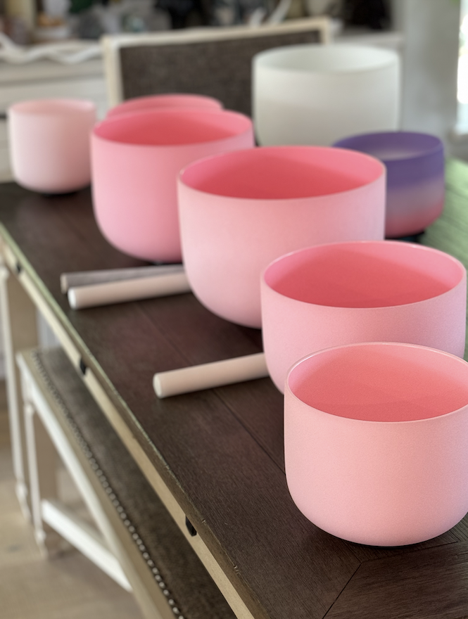 A row of six singing bowls, mainly pink, arranged on a dark wooden surface in a retail setting.