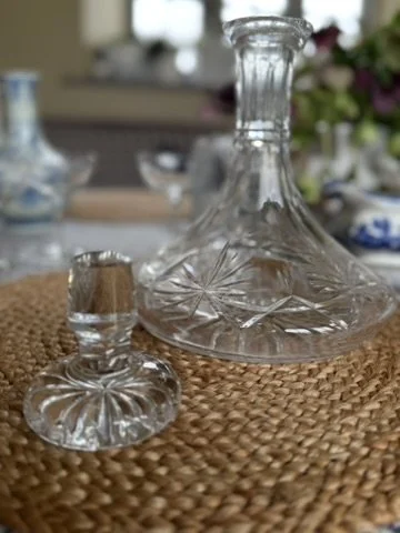 Glass decanter and stopper with intricate cut patterns on a woven surface.