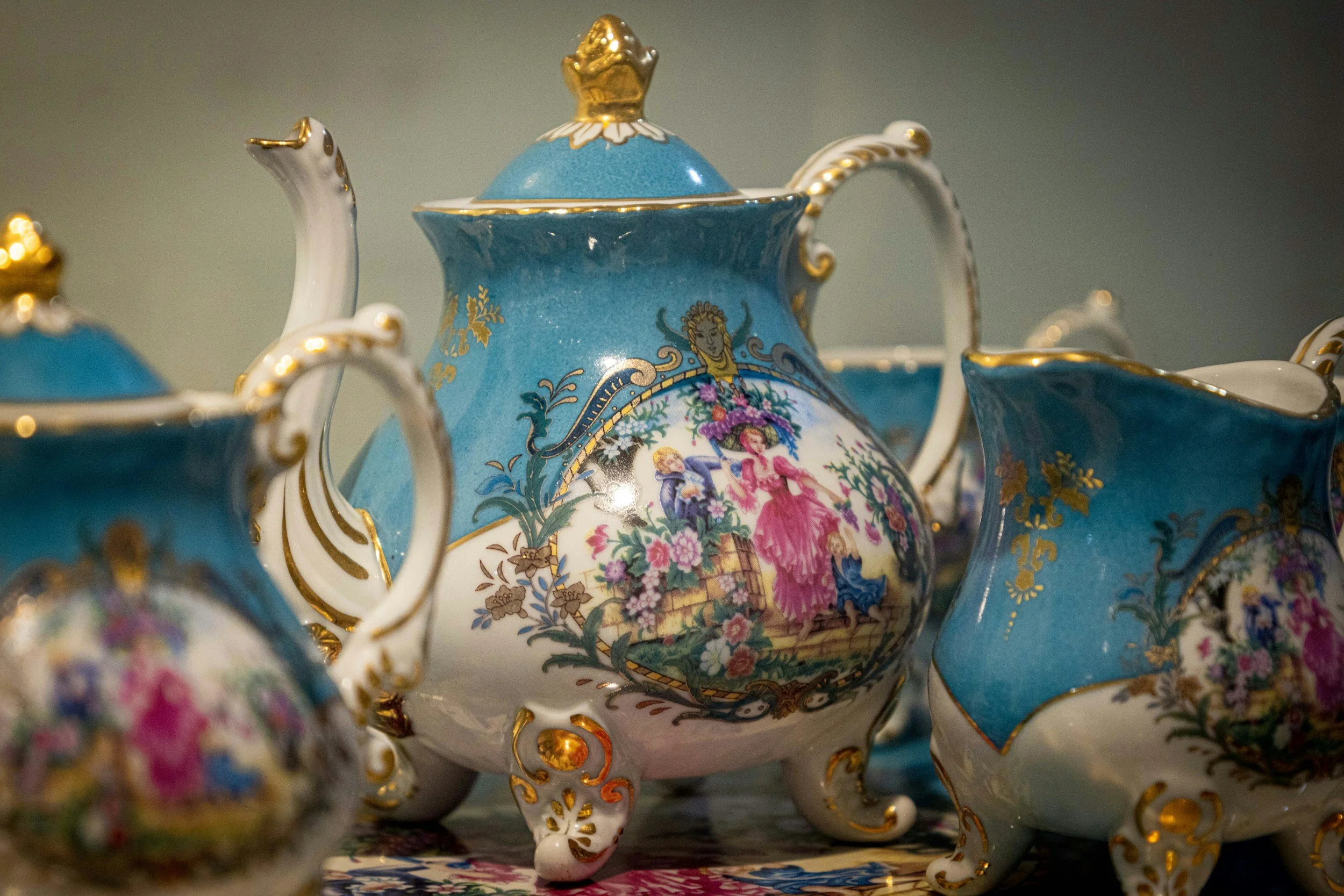 Close-up of an ornate blue porcelain teapot with gold accents and detailed painted scenes, surrounded by matching teacups.
