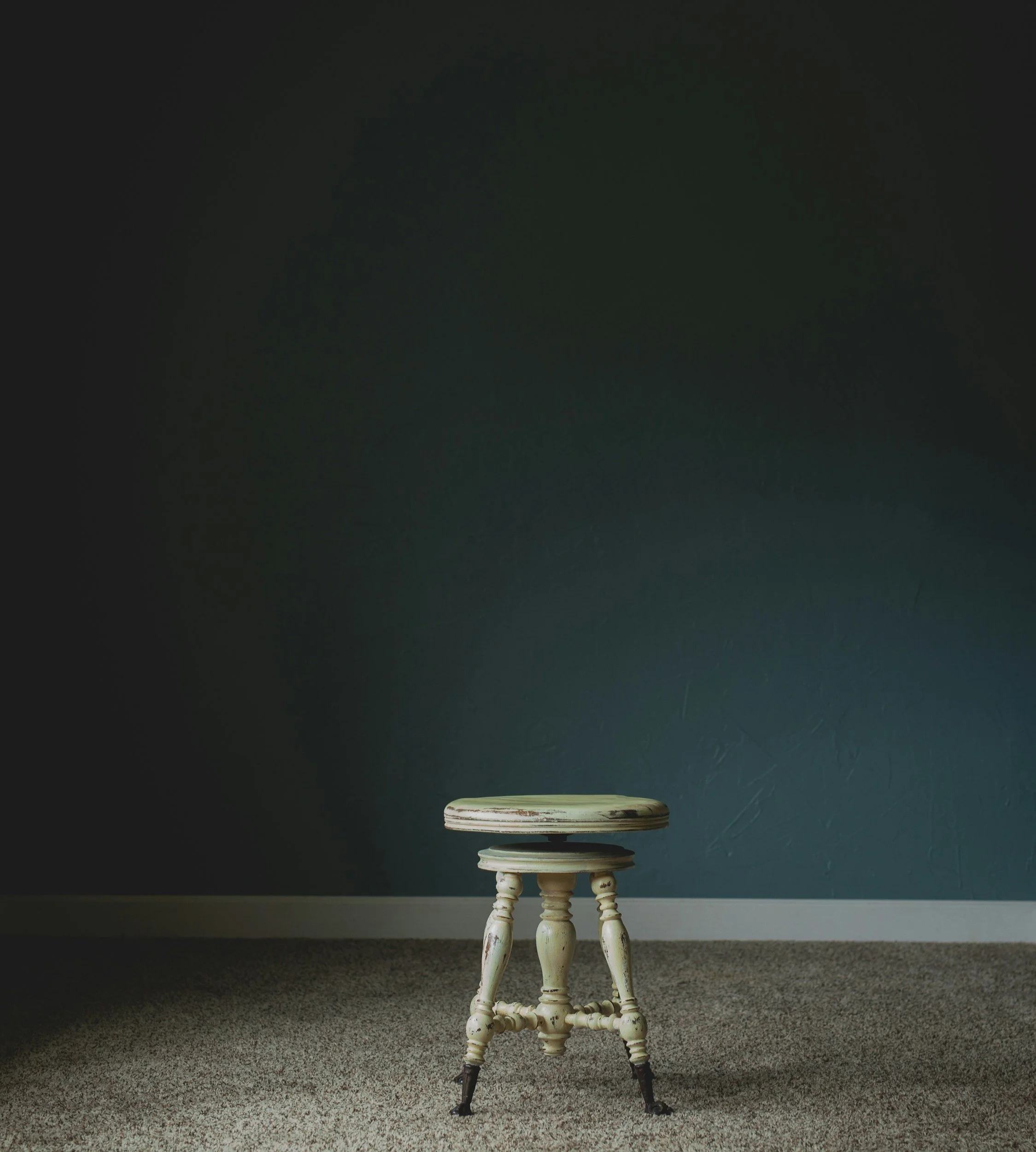 Three wooden stools stacked vertically, placed on a carpeted floor against a dark wall.
