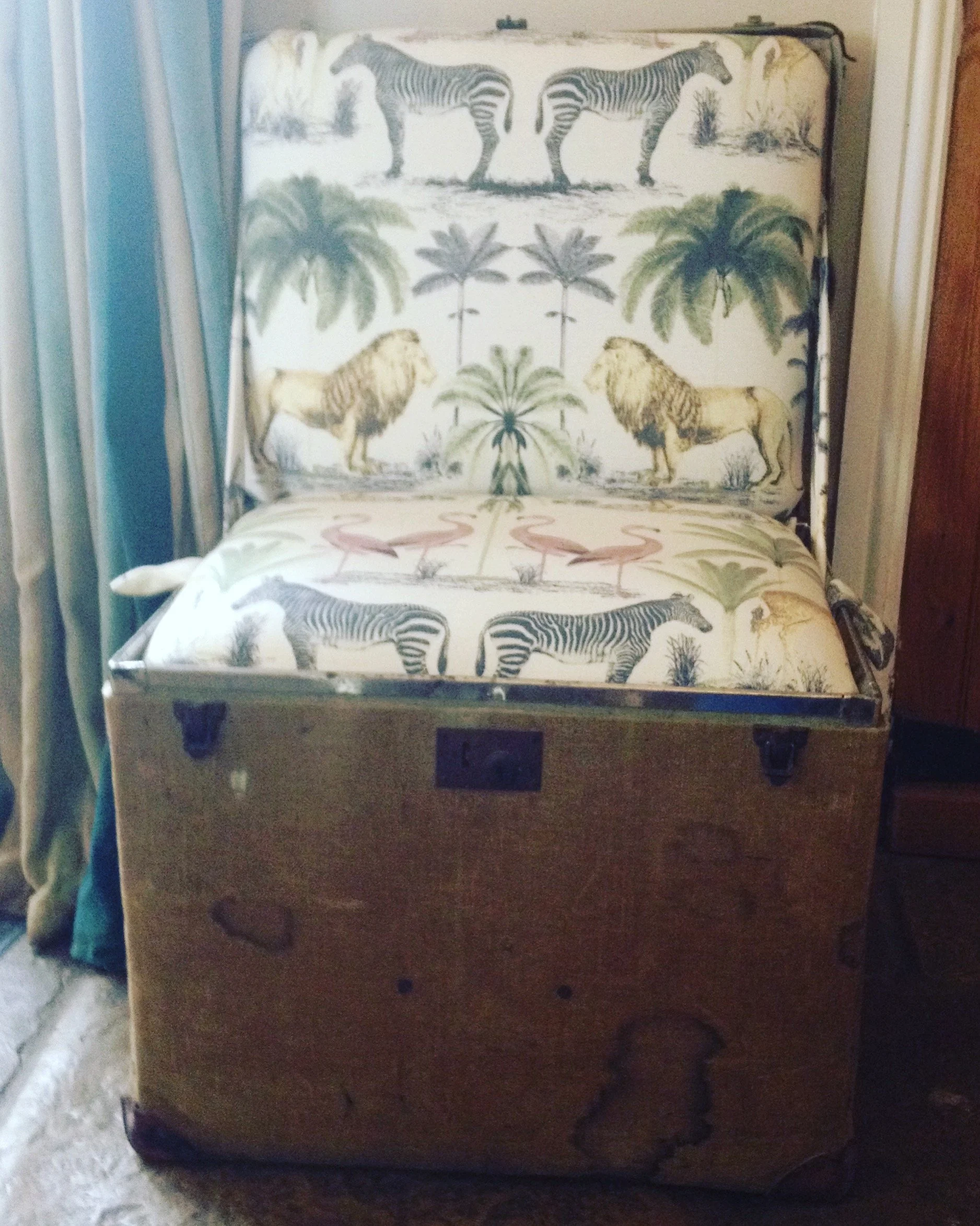 An old wooden suitcase with a vintage illustration of zebras, lions, flamingos, and palm trees, featuring a safari scene.