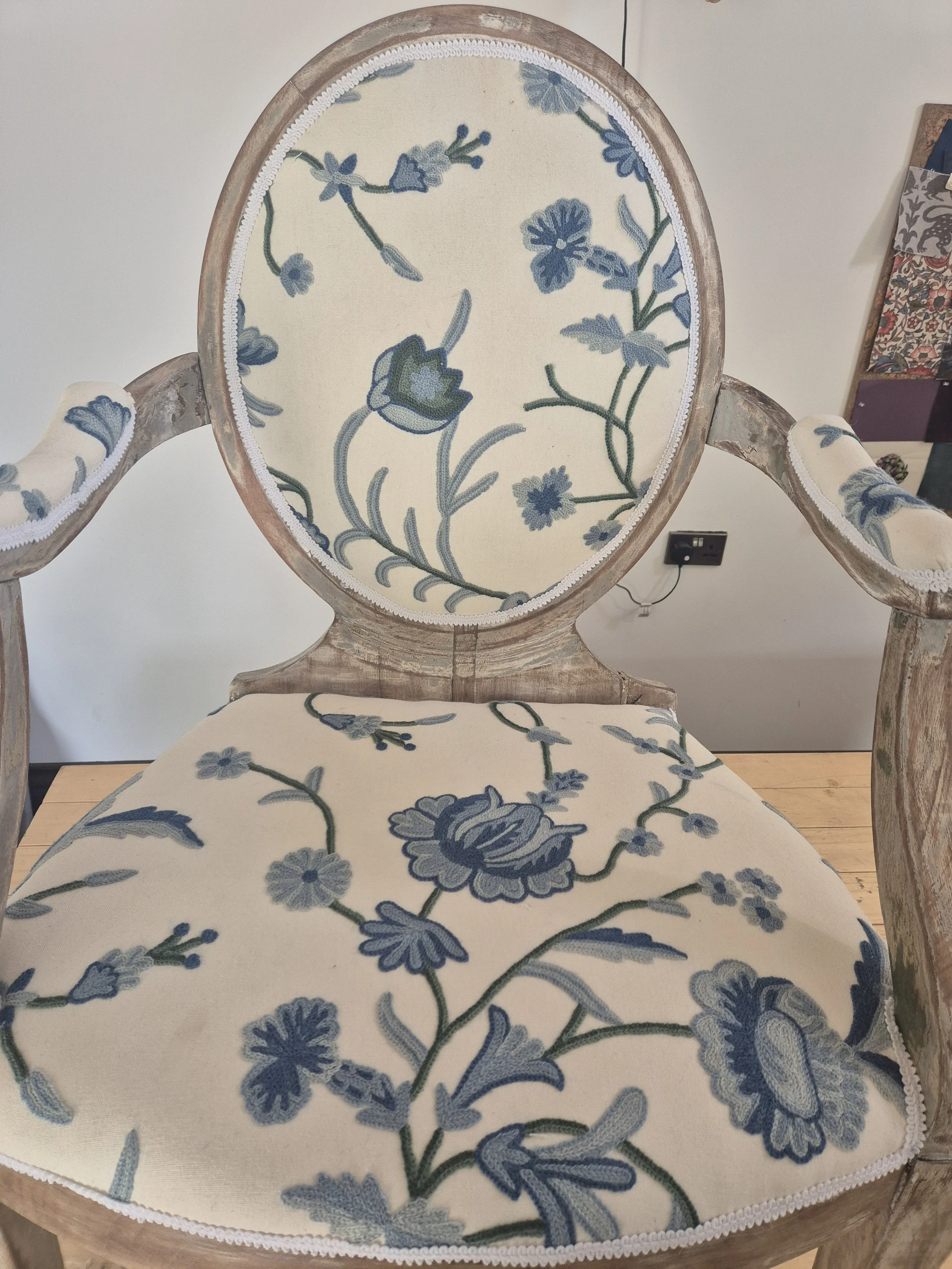A vintage wooden chair with floral upholstery featuring blue flowers and green stems on a cream background, with detailed white trim around the edges.