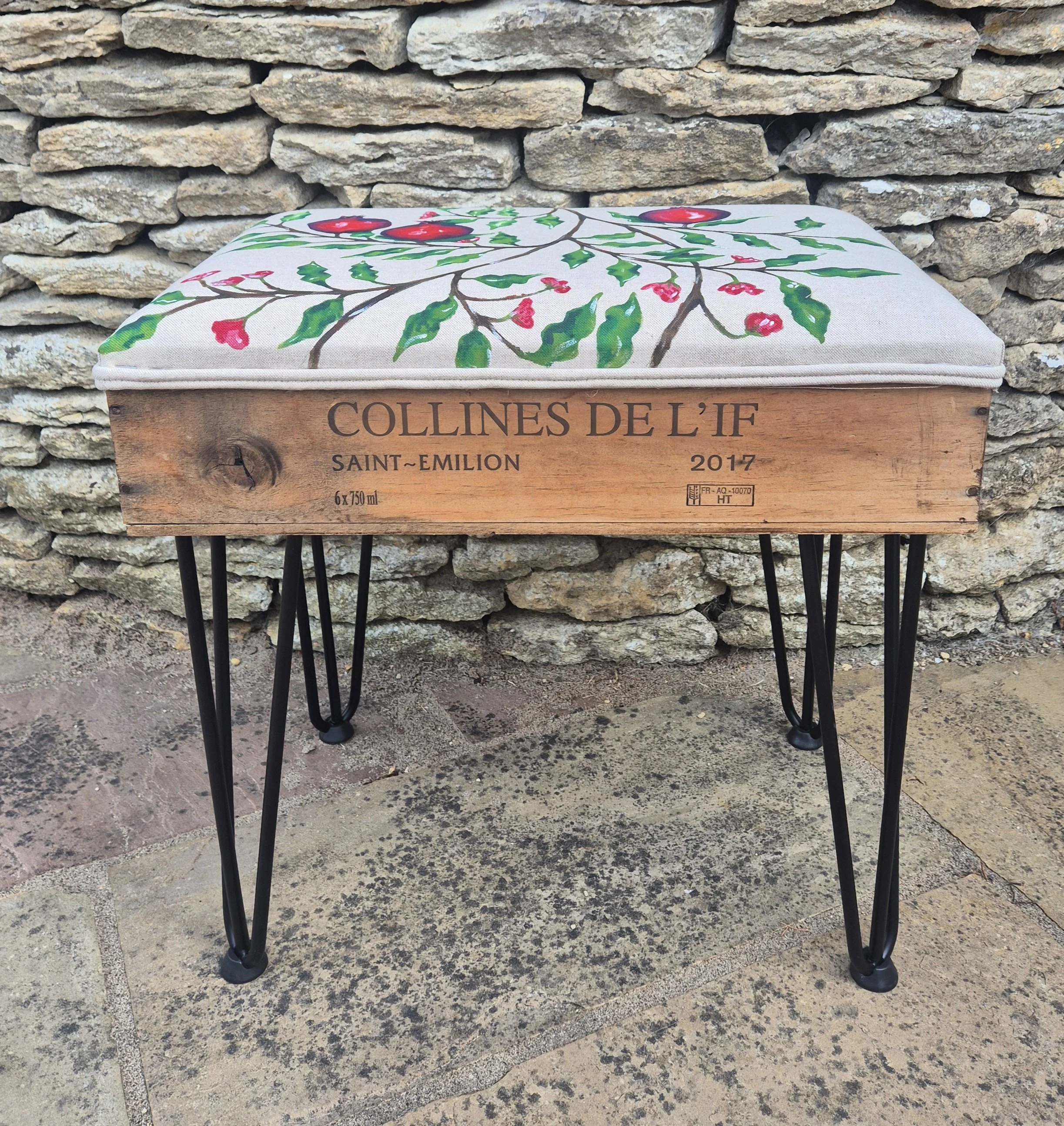 A wooden box with painted holly berries and leaves on a cushion on top. The box has text that reads 'COLLINES DE L'IF ST. EMILION 2017'.
