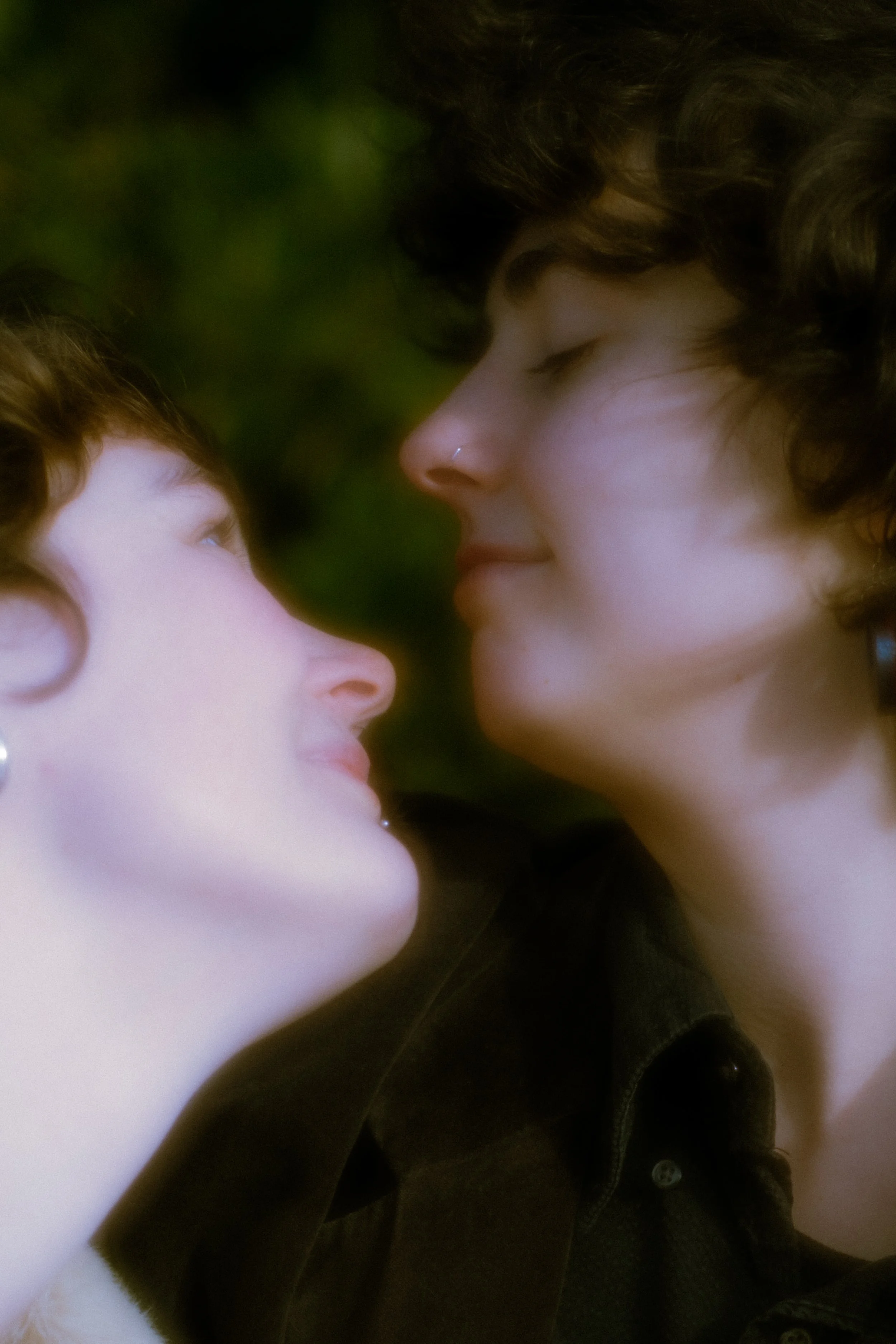A close-up photo of two women facing each other with their eyes closed, about to kiss, against a blurred green background.